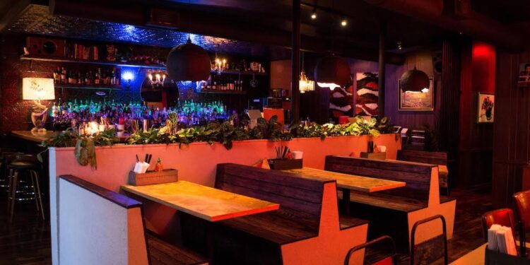 Interior of Bon Ton restaurant in Midtown Atlanta with pink walls, patterned tablecloths and hanging lights