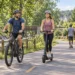 AI-generated illustration of helmeted adults riding an e-bike and e-scooter on a suburban shared-use path.